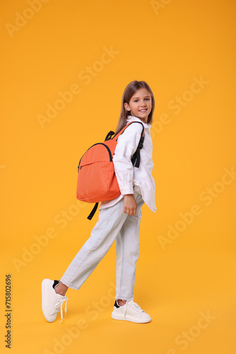 Happy schoolgirl with backpack on orange background © New Africa
