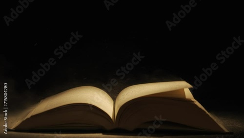 Close up studio shot of old retro hardcover book on dark background in warm light. Old vintage book laying,wind turning pages.