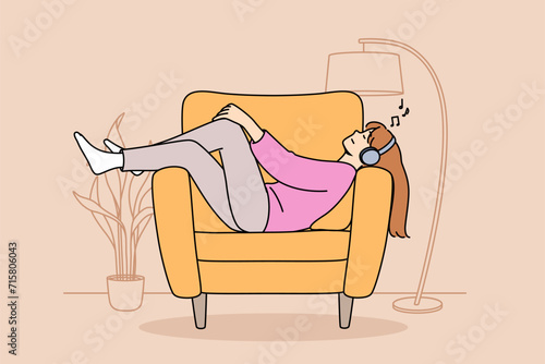 Relaxed woman wearing headphones lies on sofa, listening to music and relaxing after hard day at work. Girl enjoys popular youth music from personal playlist or educational audiobook