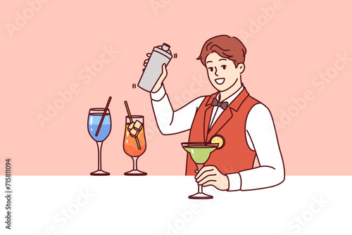 Man bartender prepares cocktail with addition alcohol and syrup with ice, inviting guests to party in nightclub. Bartender guy holds out glass of mojito with slice lime and looks at screen with smile