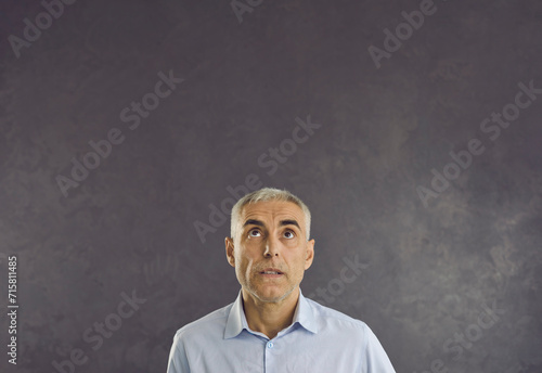 Pensive serious middle-aged Caucasian man on black studio background look up at blank empty copy space. Pensive male think consider advertising sale deal or promotion discount. Copyspace, ad.