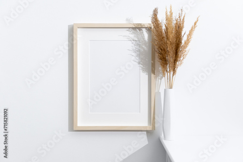 Wooden portrait frame mockup on white wall with dry grass decoration, copy space for design presentation