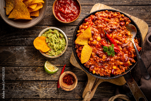 Mexican hot chili con carne in a pan with tortilla chips on dark background, top view photo