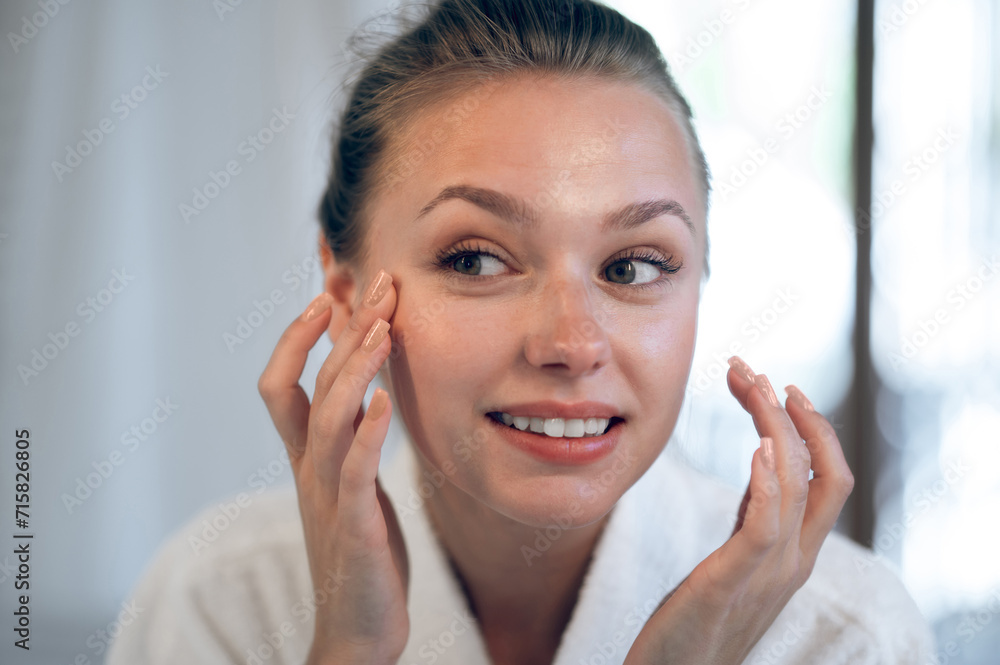 Young smiling woman applying cream on her face Young smiling woman applying cream on her face