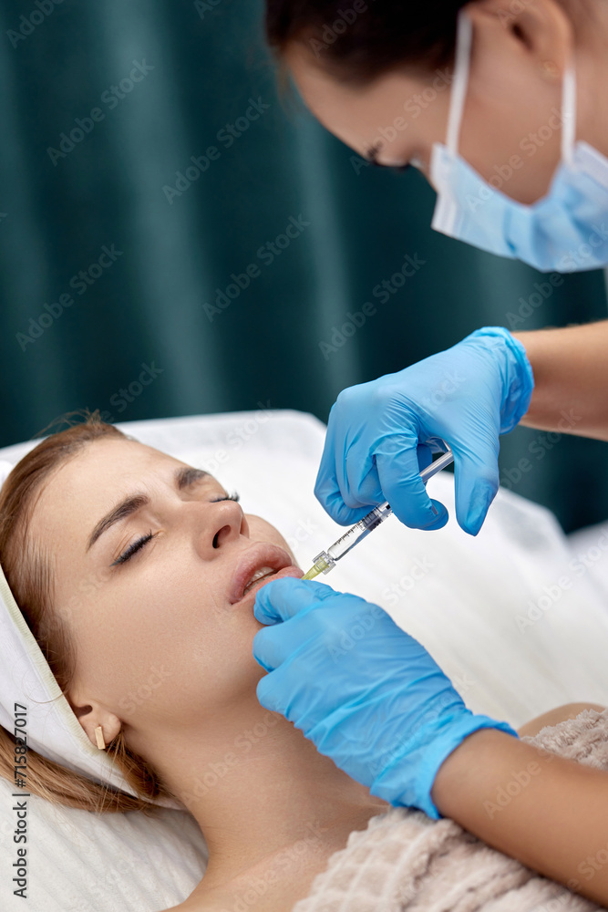 Fototapeta premium beautician makes injections to enlarge the lips of beautiful woman. procedure lip augmentation