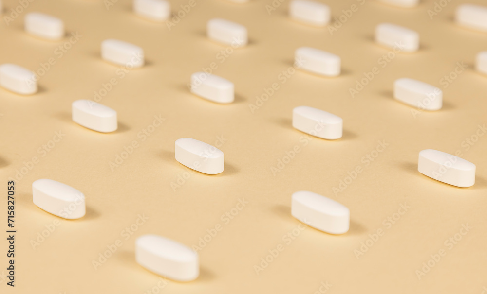 Close-up of a pattern of white pills on a beige background. Close-up of a pattern of white pills on a beige background.