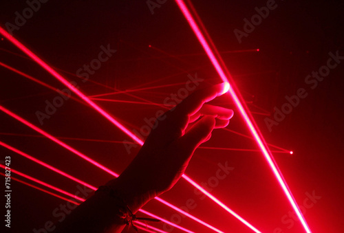 close-up hand touching the red line of a laser beam in a dark room.