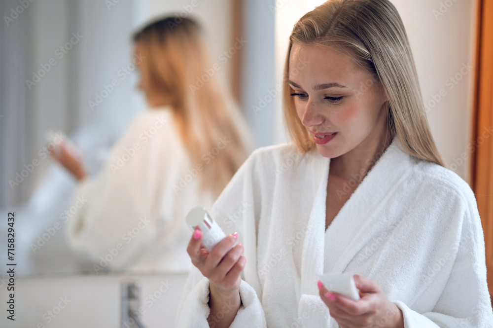 Woman in white bath robe holding face cream in hands Woman in white bath robe holding face cream in hands