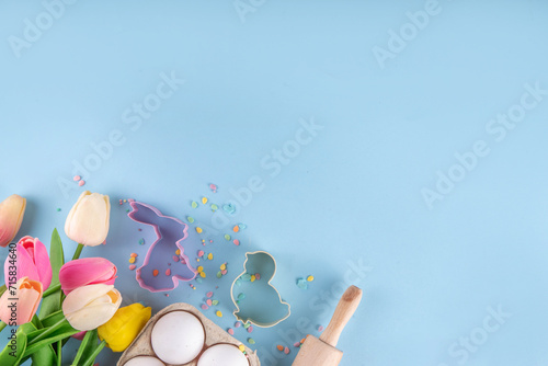 Easter baking background, ingredient for making Easter cookies, cakes, dessert with Easter chocolate eggs, sugar sprinkles, baking ingredients, flour, egg, milk, rolling pin, spring flowers top view photo