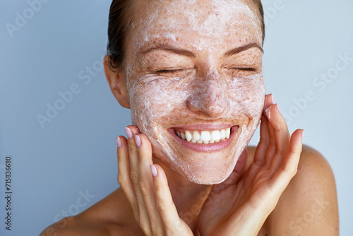 Overjoyed young woman with a freckles skin care beauty portrait.  Applying white peeling cosmetic product to whole her face. Dermatology. Exfoliating photo
