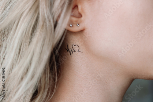 Temporary mini tattoo in the form of a heart and a cardiogram on the young woman's neck under ear photo