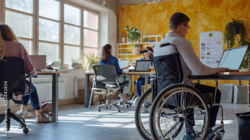 Obraz premium personne handicapée en fauteuil roulant travaillant sur son ordinateur dans un open space avec d'autres personnes valides 