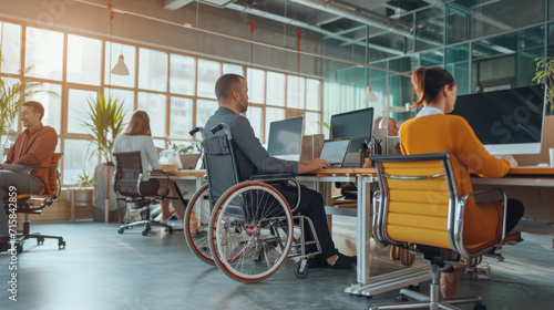 personne handicapée en fauteuil roulant travaillant sur son ordinateur dans un open space avec d'autres personnes valides  © Sébastien Jouve