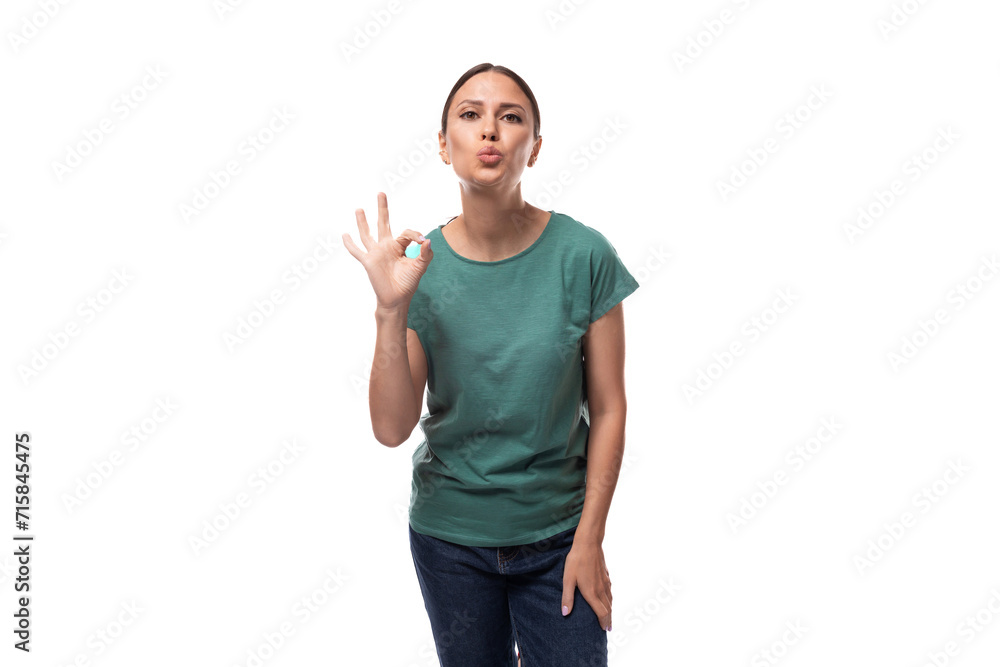 young charming brunette lady with a ponytail dressed in a green t-shirt and jeans shows a gesture of ok young charming brunette lady with a ponytail dressed in a green t-shirt and jeans shows a gesture of ok