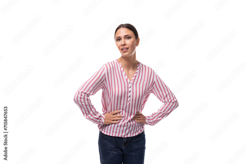 young slender well-groomed brunette leader woman with a ponytail hairstyle dressed in a striped blouse holds her hands on her waist young slender well-groomed brunette leader woman with a ponytail hairstyle dressed in a striped blouse holds her hands on her waist