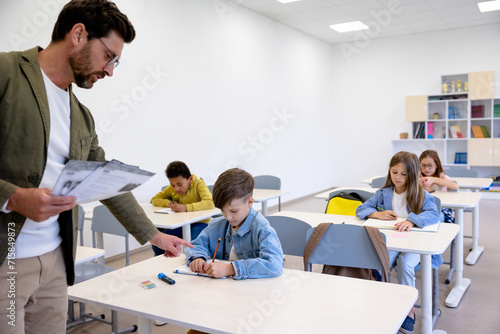Male giving tasks on paper to pupils in classroom.