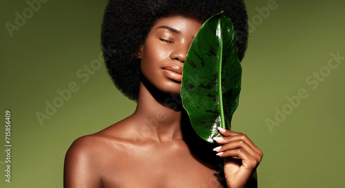 Organic natural cosmetics concept. Beauty portrait of young beautiful african american woman with posing with banana leaf curly hair against green exotixc plants background.