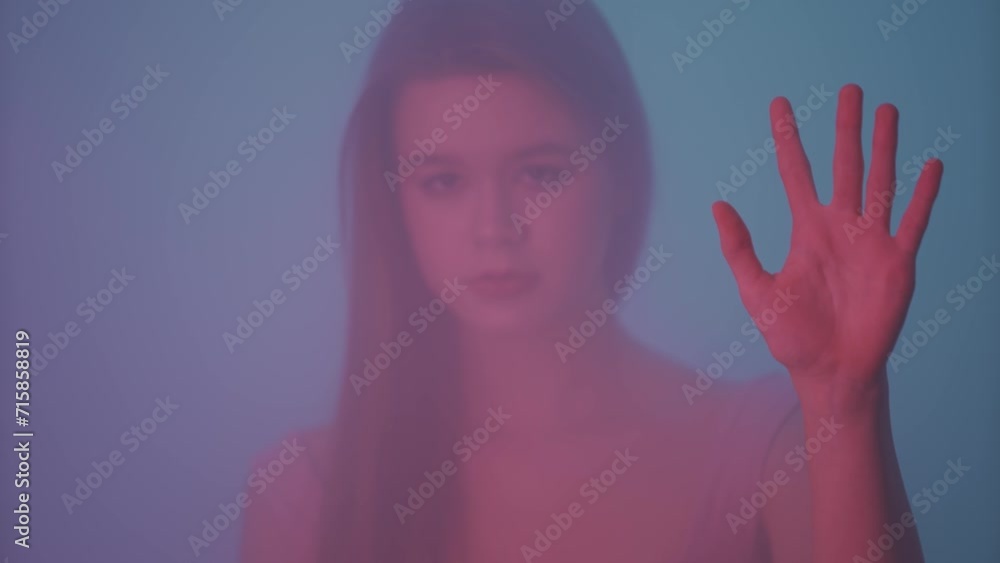 Portrait of female in neon light behind the glass window in steam and mist. Girl with makeup and hairstyle posing holding hand on glass. Portrait of female in neon light behind the glass window in steam and mist. Girl with makeup and hairstyle posing holding hand on glass.