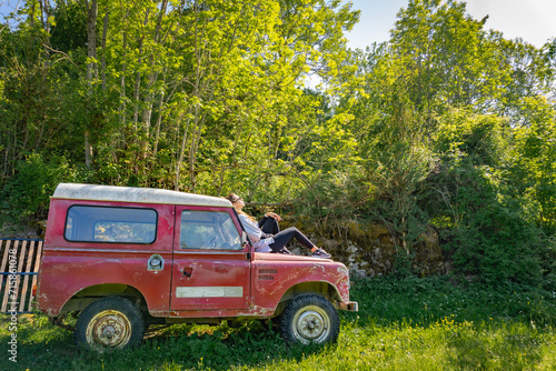 Woman sunbathing on a vintage red off-road vehicle in the forest.