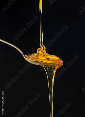 Honey falling on a spoon isolated on black background.