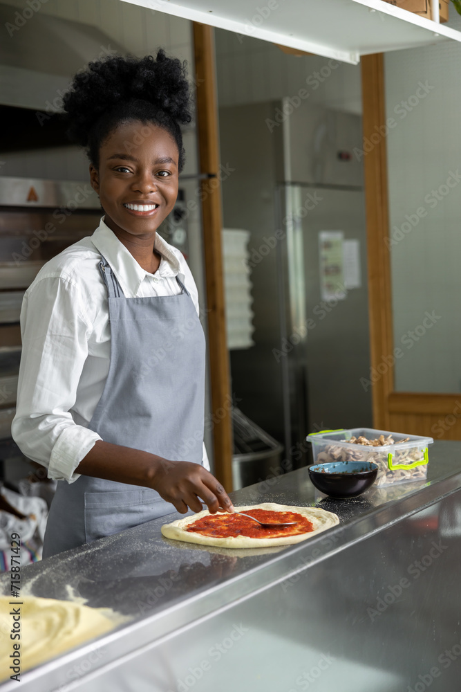 Smiling dark-skinned woman preparing pizza and looking contented Smiling dark-skinned woman preparing pizza and looking contented
