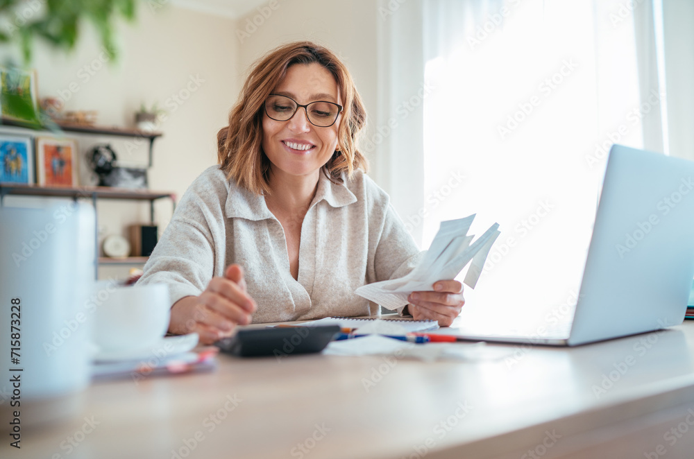 Beautiful middle-aged woman in glasses and paper bills joyfully laughing while calculating revenue grows at home office. Small business, successful investment, bull market, money savings concept image Beautiful middle-aged woman in glasses and paper bills joyfully laughing while calculating revenue grows at home office. Small business, successful investment, bull market, money savings concept image