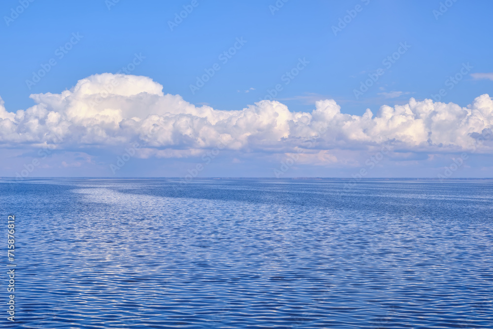 A tranquil seascape with gentle ripples on the water and billowy white clouds in the sky, their reflections dancing on the serene surface