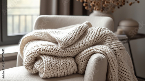 A close-up of a beautifully folded, hand-knit blanket gracefully placed on a chair, showcasing the craftsmanship and inviting texture. The soft color palette adds to the visual all