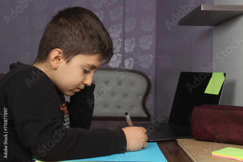 Distance learning online education. A schoolboy boy studies at home and does school homework. Bored student trying to write a composition. Stay at home concept idea. 