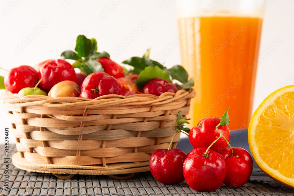 Fresh acerola juice in a glass cup in a bamboo place mat with sliced oranges and acerola fruits front view Fresh acerola juice in a glass cup in a bamboo place mat with sliced oranges and acerola fruits front view