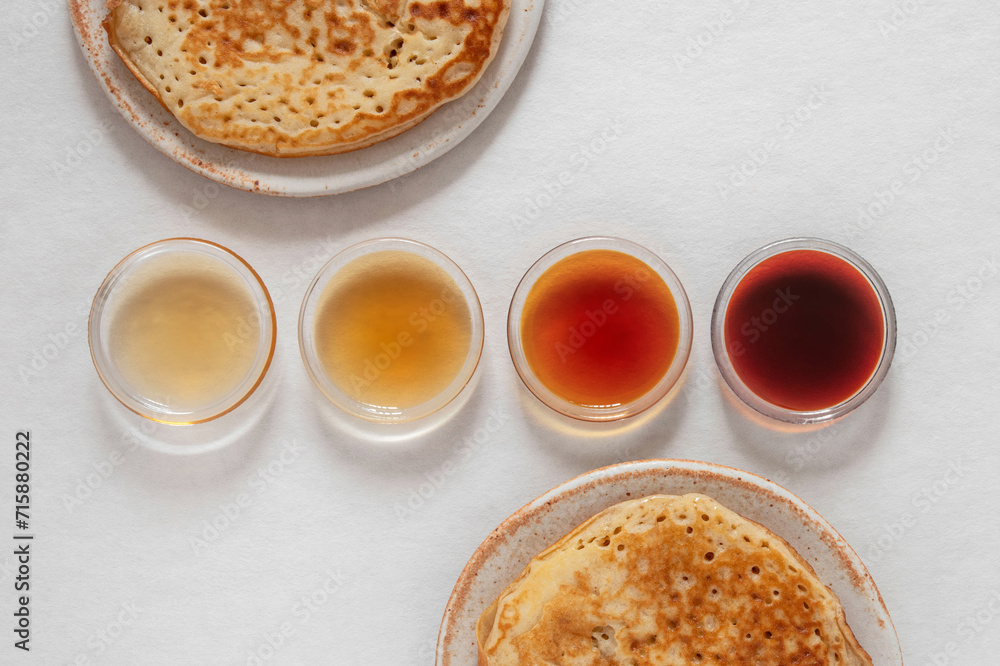 Different classes of maple syrups in different colours in glass bowls with pancakes next to them Different classes of maple syrups in different colours in glass bowls with pancakes next to them