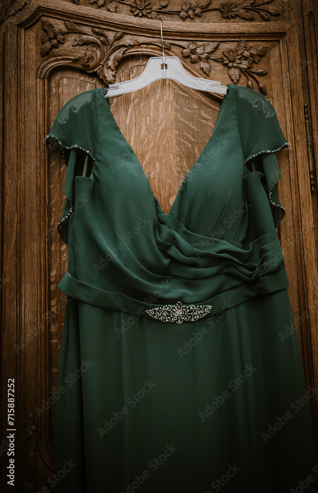 green bridesmaid or formal dress hanging on a wooden wardrobe
