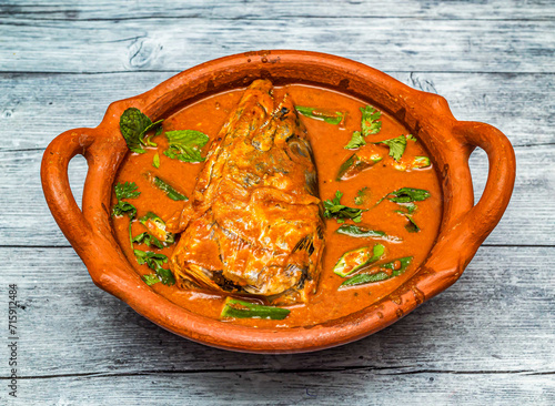 fish head curry served in clay pot isolated on wooden table top view of indian spicy food photo