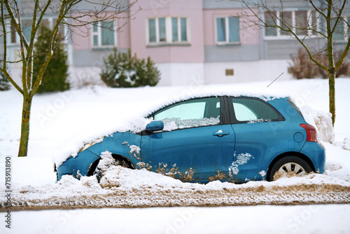 Snow covered car stuck at roadside after snow removal works. Stuck car in snowdrift. Snow removal problem. Car buried in snowy parking lot after snowstrom, wheels stuck in snow and ice blockage. photo