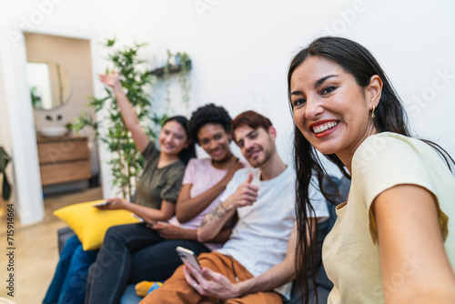 Multiracial friends sharing a joyful moment while taking a group selfie on the couch  creating memories at home.