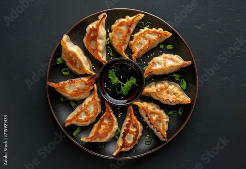 Fried gyozas on a plate plate with green onions, and soy sauce, isolated on a dark table, top view