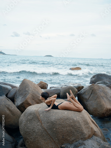 Summer Beauty: A Sensual, Slim Model in Sexy Swimwear Poses on a Beach Rock, Savoring a Paradise Vacation