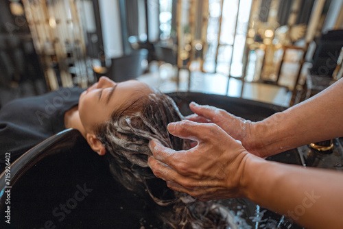 Asian woman lying down on salon washing bed getting hair washed in hair salon by stylist, Hairdresser shampoo the customer hair then washing hair photo