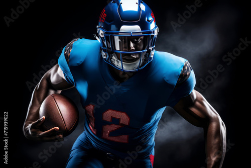 Portrait of American football player running with the ball. Muscular African American athlete in a blue and red uniform with an ovoid ball in a dynamic pose. Isolated on black background. photo