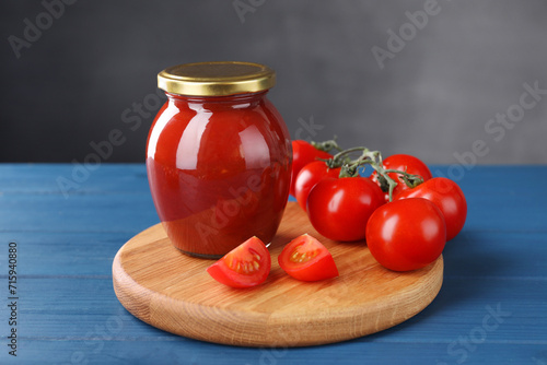 Organic ketchup in jar and fresh tomatoes on blue wooden table. Tomato sauce