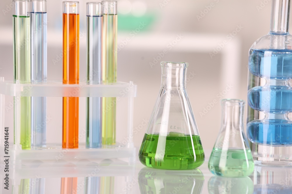 Laboratory analysis. Different glassware with liquids on white table against blurred background Laboratory analysis. Different glassware with liquids on white table against blurred background