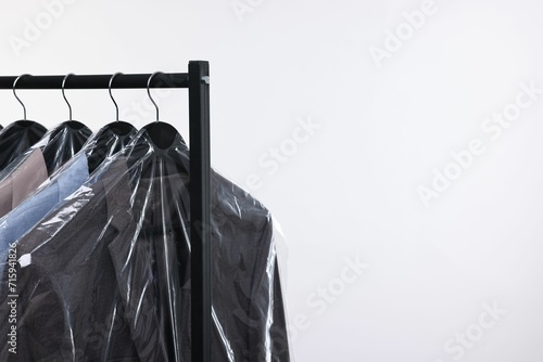 Dry-cleaning service. Many different clothes in plastic bags hanging on rack against white background, space for text photo