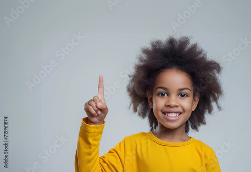 Attractive girl pointing by index finger up to place for copy space. Positive young good looking girl n with Afro hairstyle, indicates with both index fingers, wears casual yellow sweater, feels pleas photo