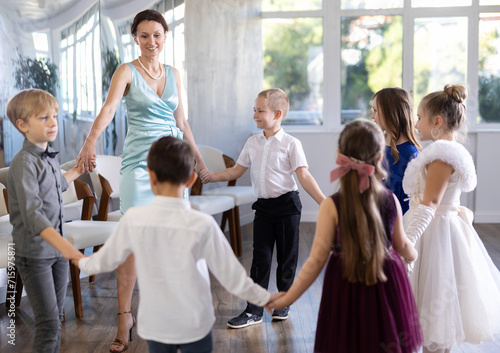Cheerful junior schoolchildren in party dresses having fun dancing in circle with female pedagogue photo