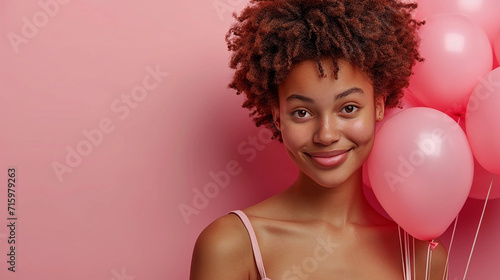 Beautiful black girl with pink air balloons over pink background. Happy Valentines day. Joyful model smiling and holding ballons in shape of heart. © litts