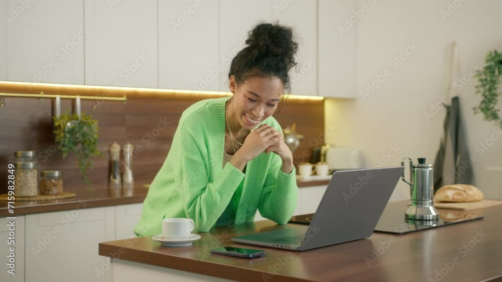 Nice mom communicating with kids from modern kitchen. Woman of color in light green cardigan on family video call. Pleasant biracial house wife with dark skin and curly hair talking to laptop camera Nice mom communicating with kids from modern kitchen. Woman of color in light green cardigan on family video call. Pleasant biracial house wife with dark skin and curly hair talking to laptop camera