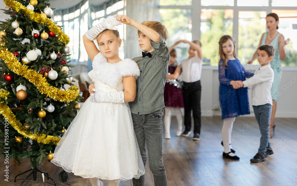Christmas ball - beautifully dressed children dance the Viennese waltz near the New Year tree