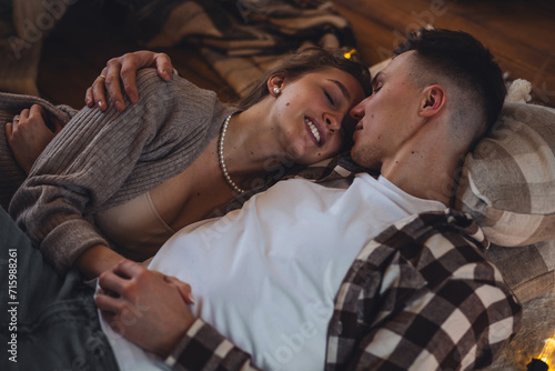 Cozy evening in the countryside house with fireplace. Young beautiful loving couple, man and woman spending time together on saint Valentine's Day, kissing, embracing. Romantic surprise