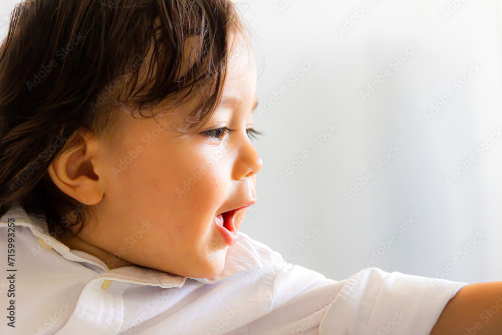 Face of Hispanic Latino baby sitting with white shirt looking forward and raising left arm Face of Hispanic Latino baby sitting with white shirt looking forward and raising left arm