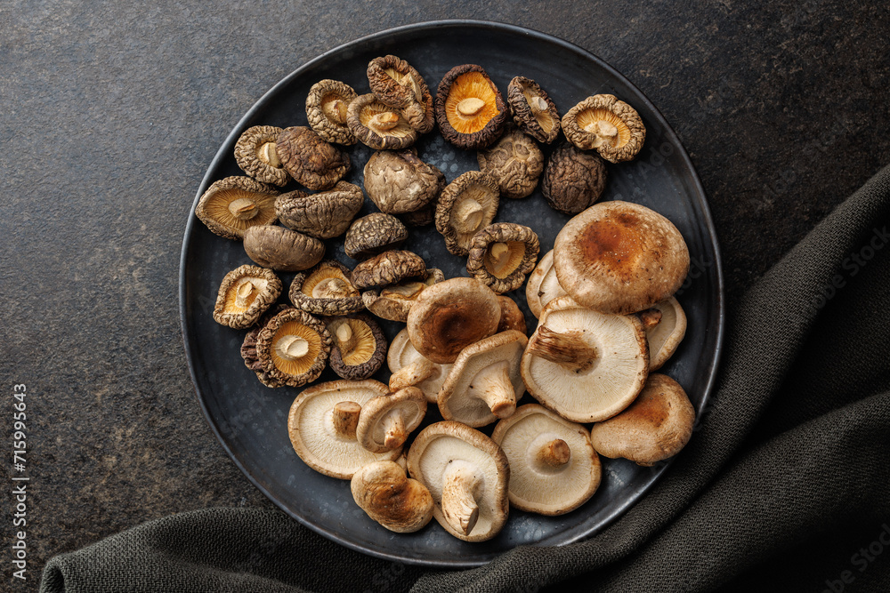 The fresh and dried shiitake mashrooms on plate on black table. Top view. The fresh and dried shiitake mashrooms on plate on black table. Top view.